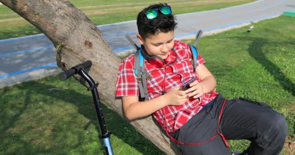 Αγόρι Νεαρή Σχολή Χρησιμοποιώντας Smartphone Και Χαλαρώσετε Στο Πάρκο Της — Αρχείο Βίντεο