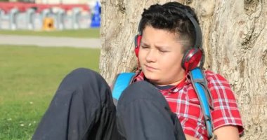 Şehir Parkı, müzik dinlemek ve rahatlatıcı bir Çimenlikte oturan kulaklık ile genç bir çocuk portresi