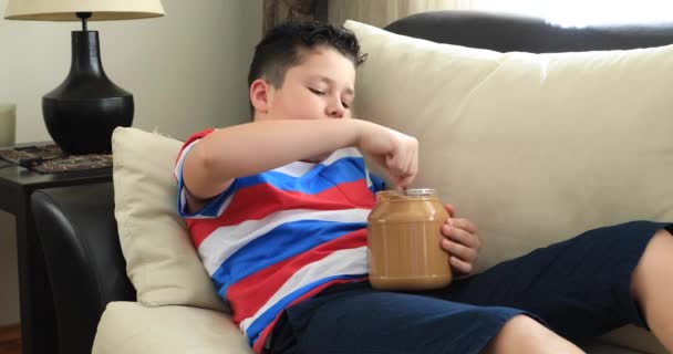 Retrato Niño Sentado Sofá Con Cuchara Comiendo Mantequilla Maní Del — Vídeo de stock