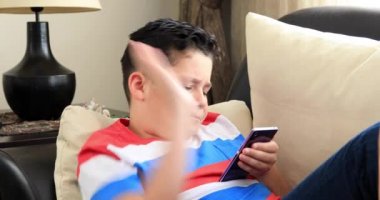 Kanepede oturan ve evde smartphone kullanarak mutlu bir varoluş çocuk portresi. Teknoloji, Internet iletişim ve insan kavramı, Smartphone bağımlılığı