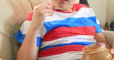 Kavanozdan fıstık ezmesi yemek kaşık ile bir kanepede oturan bir çocuk portresi