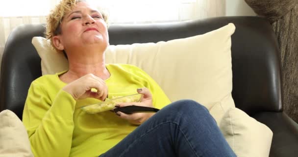 Портрет Расслабленной Блондинки Сидящей Диване Поедающей Нездоровую Пищу Смотрящей Телевизор — стоковое видео