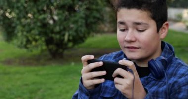 Portrait of a handsome teen boy sitting on the park bench alone Kid watching to screen, reading, typing, playing games. Technology, internet communication and people concept, Smartphone addiction