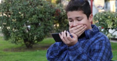 Portrait of a handsome teen boy sitting on the park bench alone Kid watching to screen, reading, typing, playing games. Technology, internet communication and people concept, Smartphone addiction