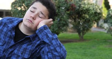 Portrait of a young handsome teenager sitting on park bench alone