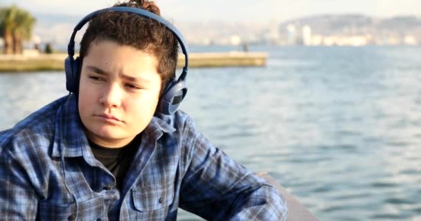 Retrato Adolescente Triste Guapo Con Auriculares Sentados Orilla Del Mar — Vídeos de Stock