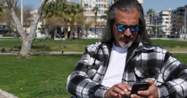 Orta yaşlı bir adam şehir parkında akıllı telefondan fotoğraf çekiyor.