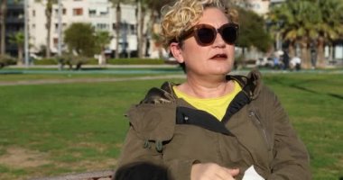 Alerji semptomlu beyaz bir kadın parkta oturmuş burnunu siliyor..