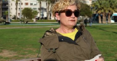 Alerji belirtileri gösteren orta yaşlı bir kadın burnunu siliyor ve parkta elini temizliyor.