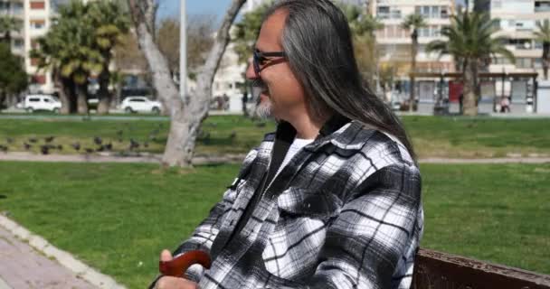 一个英俊的中年黑发男子坐在公园长椅上 望着别处的画像 — 图库视频影像
