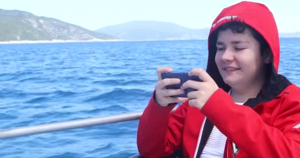 在阳光明媚的春日乘坐游艇和玩智能手机的高加索少年的肖像 — 图库视频影像