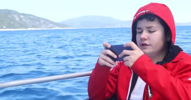 在阳光明媚的春日乘坐游艇和玩智能手机的高加索少年的肖像 — 图库视频影像