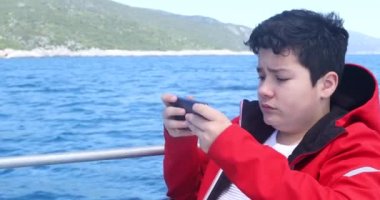 Beyaz bir gencin portresi yatla seyahat ediyor ve güneşli bahar gününde akıllı telefonla video oyunu oynuyor.