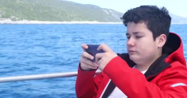 Beyaz bir gencin portresi yatla seyahat ediyor ve güneşli bahar gününde akıllı telefonla video oyunu oynuyor.