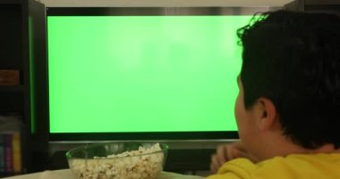 Kanepede oturmuş, yeşil ekran televizyon seyreden ve evde atıştırmalık yiyen bir çocuğun arka planı.