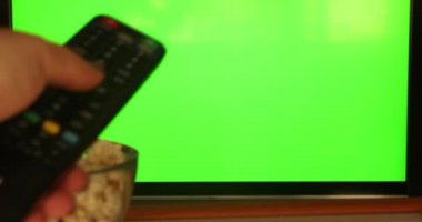 Düz yeşil ekrandaki kanalları uzaktan kumandayla kontrol eden bir kadın. Atıştırmalıklı televizyon izliyor.