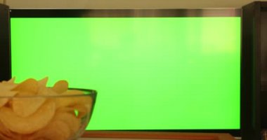 Düz yeşil ekrandaki kanalları uzaktan kumandayla kontrol eden bir kadın. Atıştırmalıklı televizyon izliyor.