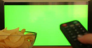 Düz yeşil ekrandaki kanalları uzaktan kumandayla kontrol eden bir kadın. Atıştırmalıklı televizyon izliyor.