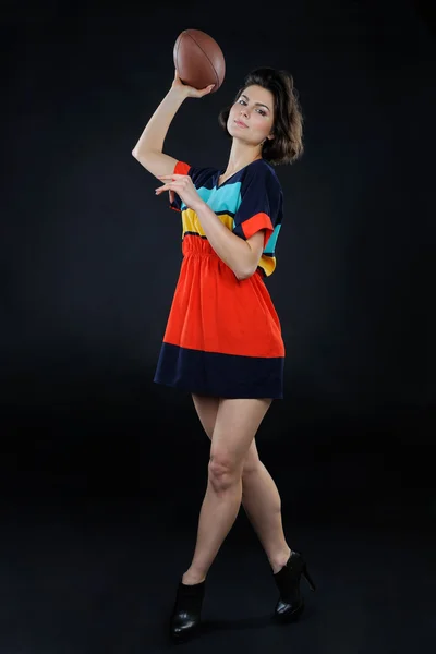 Athletic girl with a ball in colorful dress in studio on dark ba — Stock Photo, Image