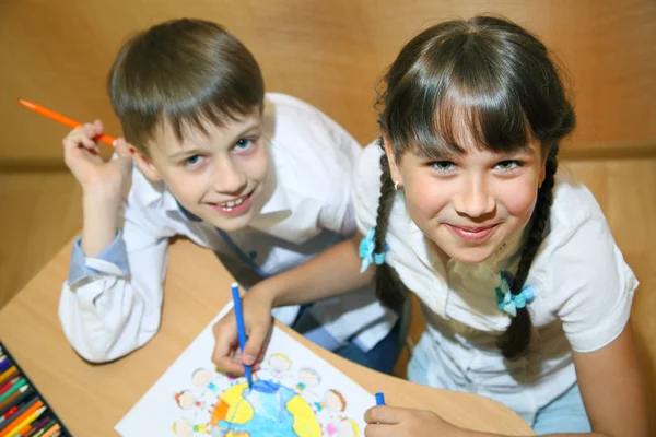 Children draw on paper. Creativity and education concept. The child paints with colored pencils on a white sheet of paper (table)