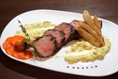 İştah açıcı biftek orta kızartma, kremalı mantar sos parçalar halinde kesin. Ahşap bir masa üzerinde beyaz tabakta servis biftek.