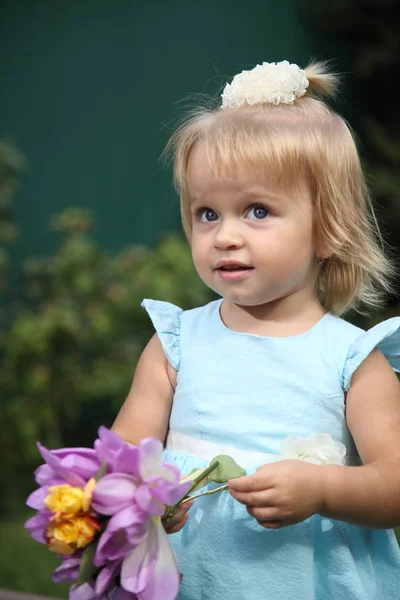 Солодка усміхнена дівчинка з довгим світлим волоссям, сидить на траві в літньому парку, крупним планом портрет на відкритому повітрі. Чарівна маленька дівчинка на траві. Маленька дівчинка в саду — стокове фото