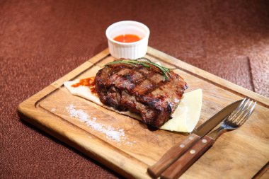 Ahşap bir tahtanın üzerinde orta pişmiş biftek, sos ve tuz..