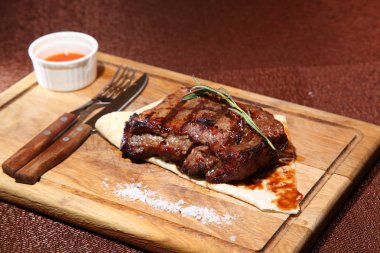 Ahşap bir tahtanın üzerinde orta pişmiş biftek, sos ve tuz..