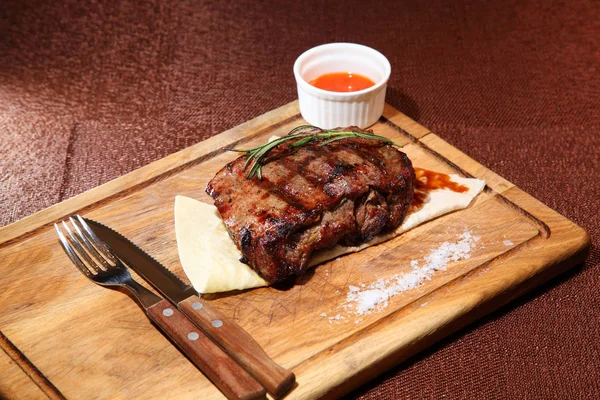 Mittelgebratenes Steak in Stücke geschnitten auf einem Holzbrett mit Sauce und Gewürzen. — Stockfoto