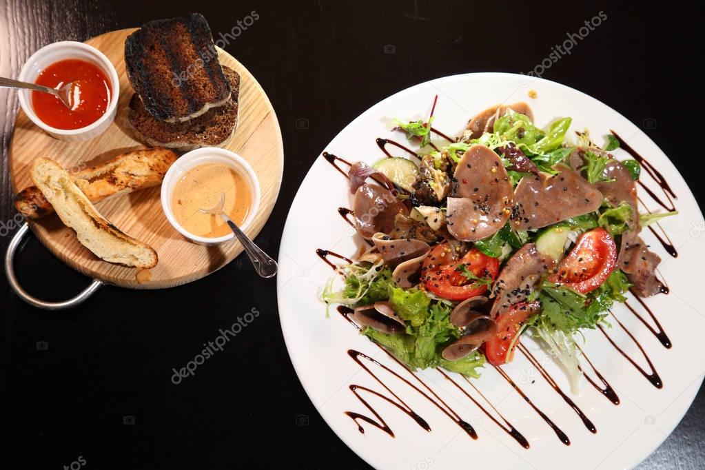Salad with beef tongue with vegetables and herbs, dressed with sauce on a white plate. 