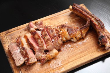 Ahşap bir tahtanın üzerinde sos ve tuzla birlikte biftek kızartılmış..