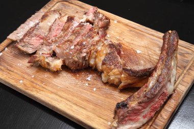 Ahşap bir tahtanın üzerinde sos ve tuzla birlikte biftek kızartılmış..