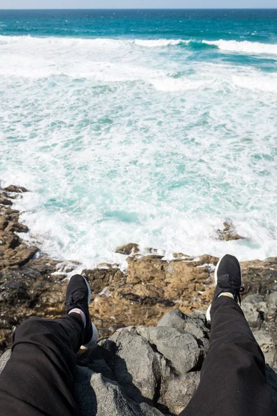 Traveller\'s feet in sneakers on a beach cliff