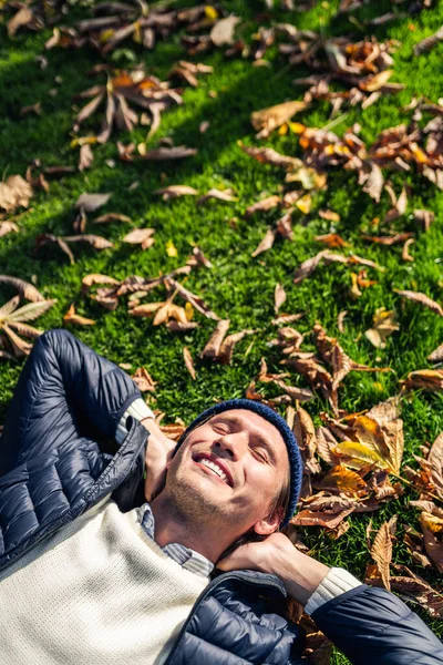 Glücklicher junger Mann entspannt sich im Park zwischen Herbstblättern. — Stockfoto