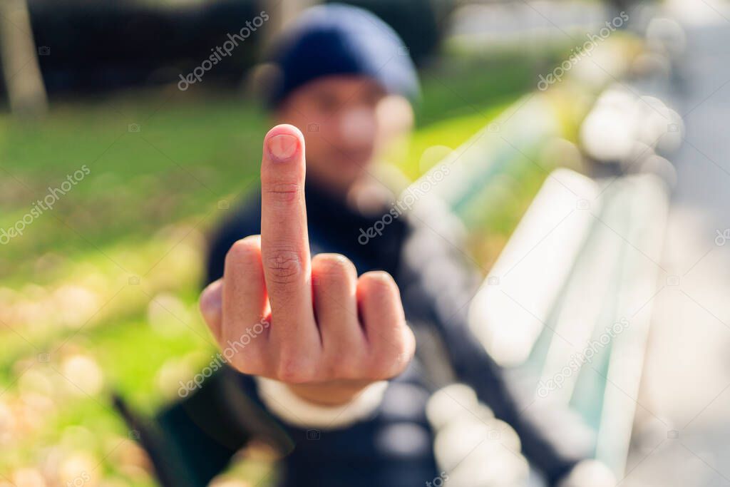 Young man showing 'fuck off' gesture while sitting on a bench