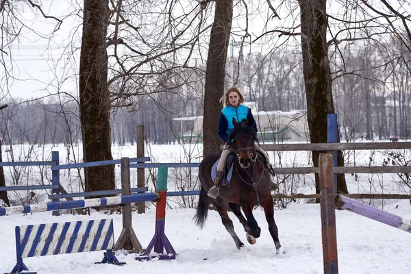 A girl on a horse  jumps  gallops. A girl trains riding a horse in a small paddock. A cloudy winter day.