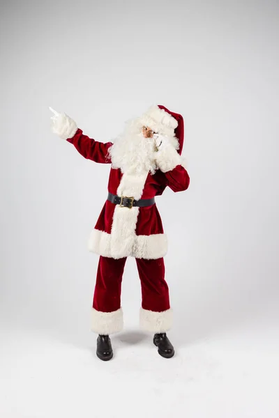 Papai Noel em óculos e traje vermelho fazer um ponto com as mãos no fundo branco e olhando para a câmera . — Fotografia de Stock