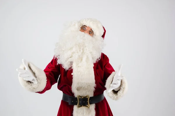 Santa Claus in eyeglasses and red costume throwing up hands on white background and looking into camera. — Stock Photo, Image