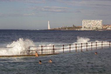 Bajamar, Tenerife, Kasım 2017: Doğal yüzme havuzunda turistler ne kadar büyük dalgaları kıyıda kırma gözlemlemek. Arka plan üzerinde dev deniz feneri ile turistik şehir Punto del Hidalgo.