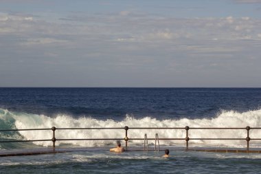 Bajamar, Tenerife, Kasım 2017: Doğal yüzme havuzunda turistler ne kadar büyük dalgaları kıyıda kırma gözlemlemek. Arka plan üzerinde dev deniz feneri ile turistik şehir Punto del Hidalgo.