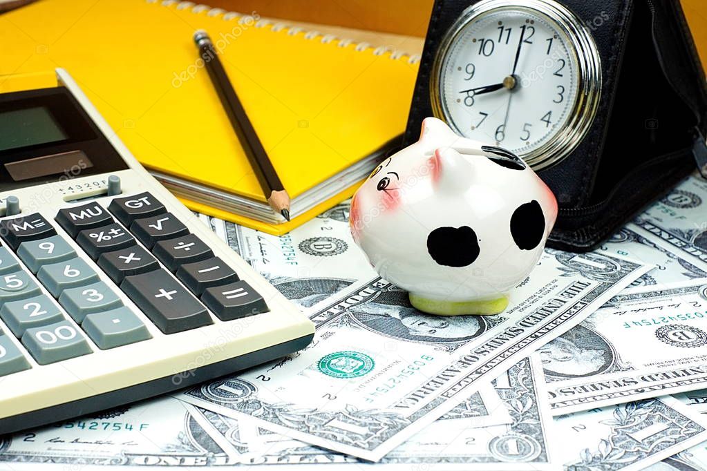 Small piggy bank and financial calculator on Piles of  US dollar