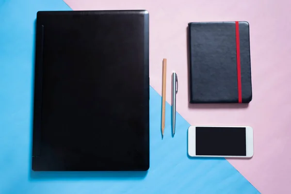 Dizüstü bilgisayarın üst görüntüsü, akıllı telefon, defter, kalem, mavi ve pembe pastel renkli fırın zemin