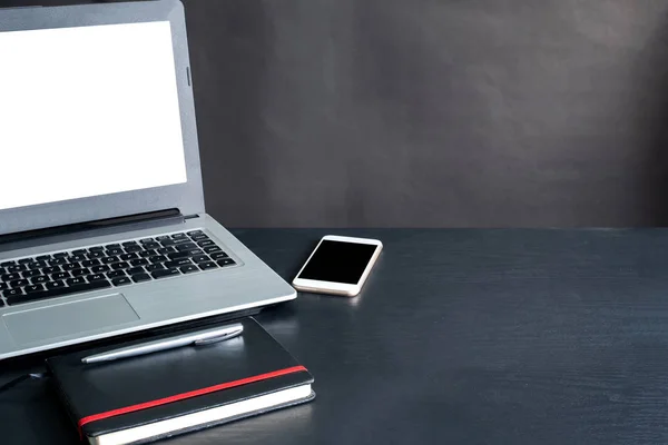 Laptop, akıllı telefon, defter, kalem, siyah arka planlı siyah ahşap masa