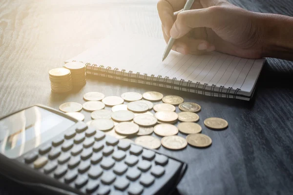 Close-up hand van de mens schrijven op notebook met rekenmachine met gouden munten, pen op zwarte tafel. Bedrijfsleven, financiën, marketing, e-commerce concept en ontwerp — Stockfoto