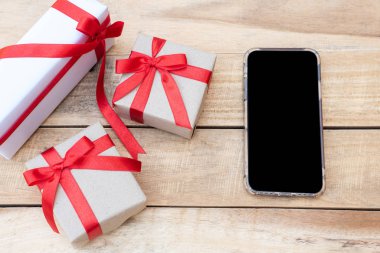Üst manzara hediye kutularını ve akıllı telefonu kapatır. Tahta masada hediye kutularıyla kırmızı kurdele, kopya alanı olan paketlenmiş klasik kutu.