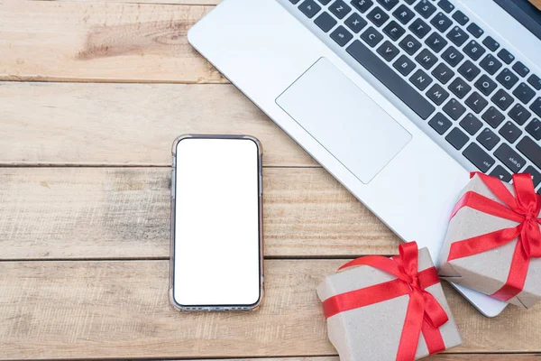 Üst manzara hediye kutuları, akıllı telefon ve dizüstü bilgisayarı kapatın. Tahta masada hediye kutularıyla kırmızı kurdele, kopya alanı olan paketlenmiş klasik kutu.