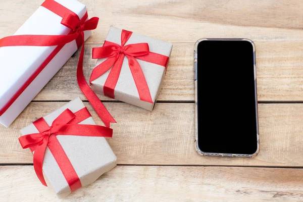 Üst manzara hediye kutularını ve akıllı telefonu kapatır. Tahta masada hediye kutularıyla kırmızı kurdele, kopya alanı olan paketlenmiş klasik kutu.