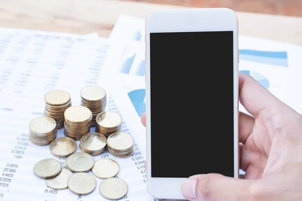 The hand of the man holding the smartphone and stack of coins on blue pastel chart paper. Business, finance, marketing, e-commerce concept and design.