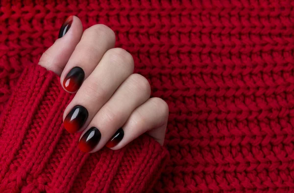 Mão feminina com pregos ombre preto vermelho gradiente em suéter — Fotografia de Stock