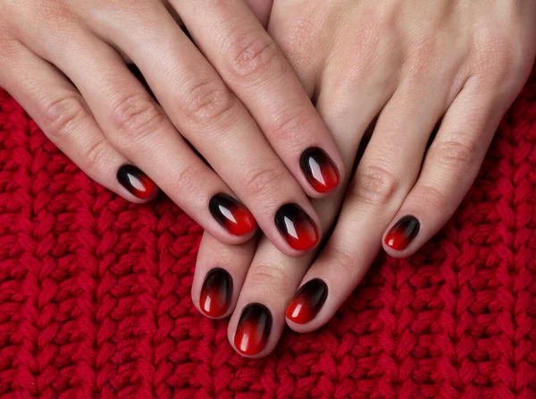 Two female hands with red black ombre gradient nails on knitted fabric — Stock Photo, Image